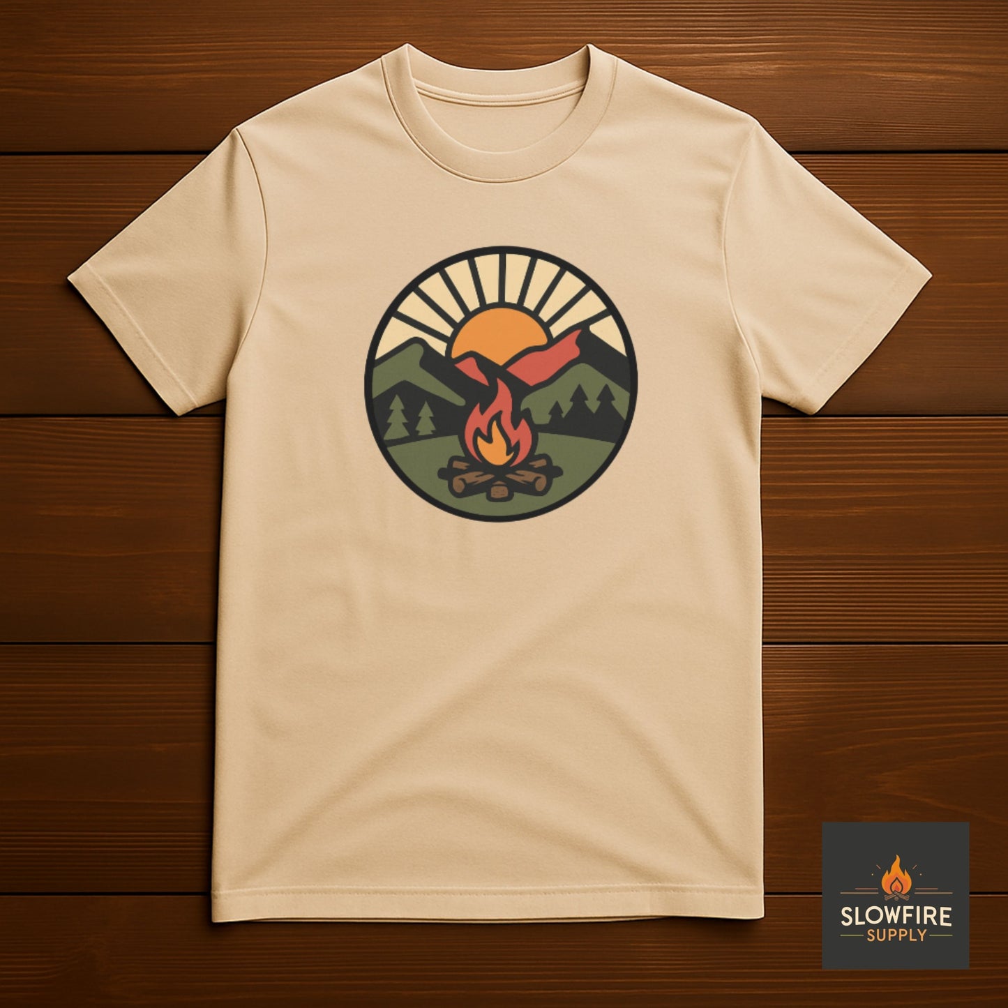 Sand colored t-shirt with a graphic design of a campfire, sunrise and mountains on a wooden background, featuring the Slowfire Supply brand.