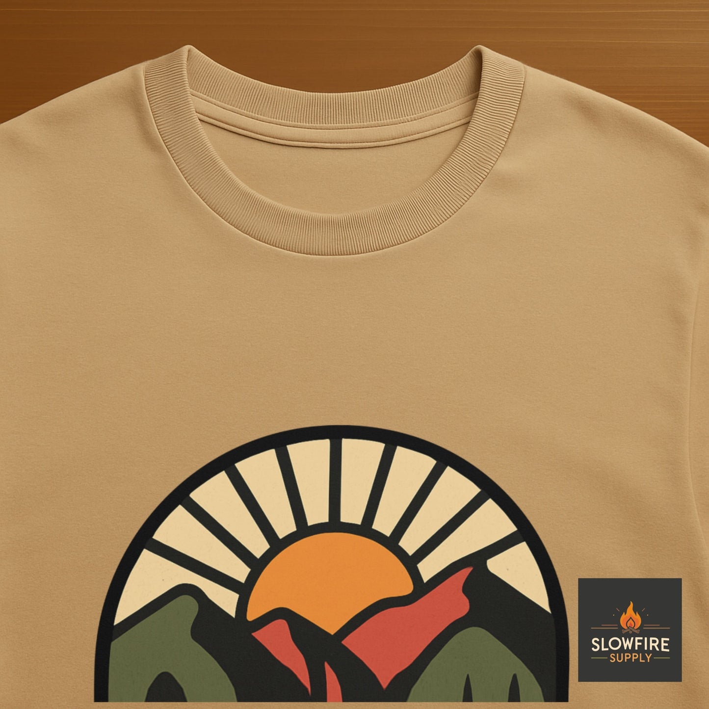 Sand colored T-Shirt with a sun and mountain graphic and Slowfire Supply logo on a wood background