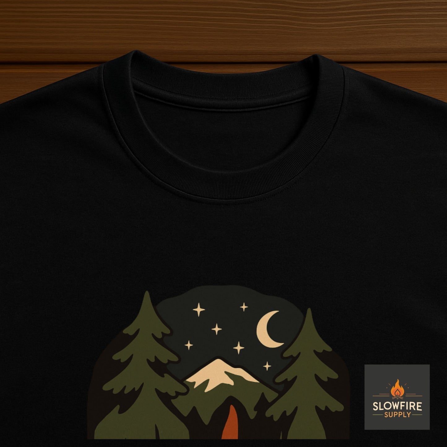Black t-shirt with a nature-themed design featuring trees, mountains, and stars on a wooden surface.