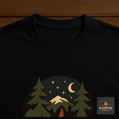 Black t-shirt with a nature-themed design featuring trees, mountains, and stars on a wooden surface.