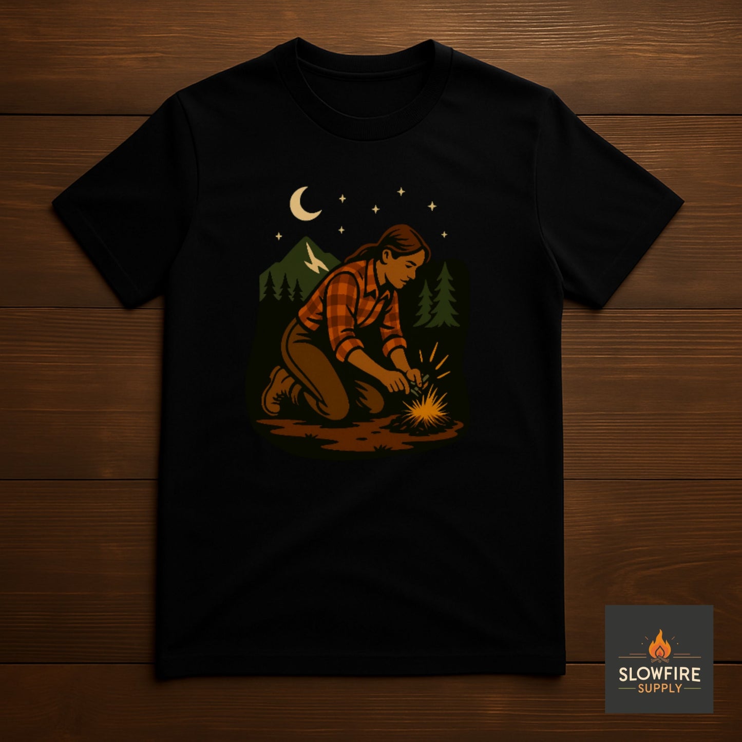Black t-shirt with a graphic of a person starting a fire in the woods, displayed on a wooden surface.