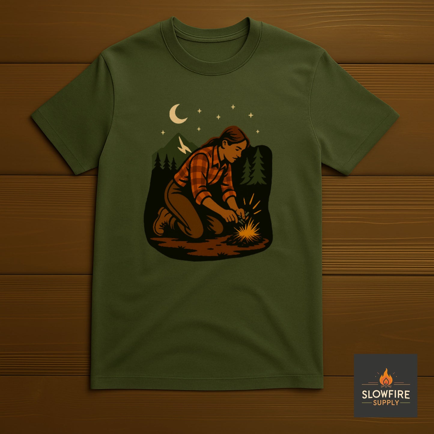 Green t-shirt with a graphic of a person building a fire in the woods, displayed on a wooden surface.