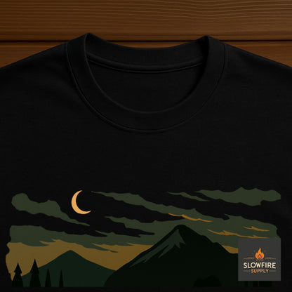 Black t-shirt with a mountain and moon design on a wooden surface